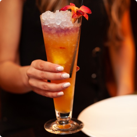 cocktail-festif-siam.jpg Une femme tient un cocktail thaïlandais coloré avec une fleur d'hibiscus.