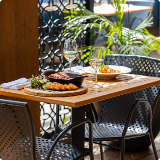 terrasse-centre-ville-montreal-siam.jpg Une table pour deux avec des plats thaïlandais traditionnels et deux verres de vin blanc sur la terrasse du centre-ville de Montréal.