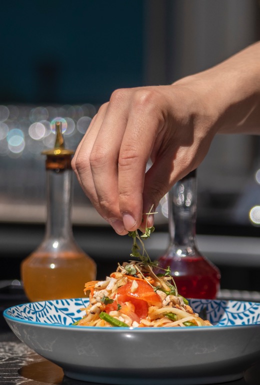 Un cuisinier du Siam dépose des micropousses de verdure sur une salade thaïlandaise.