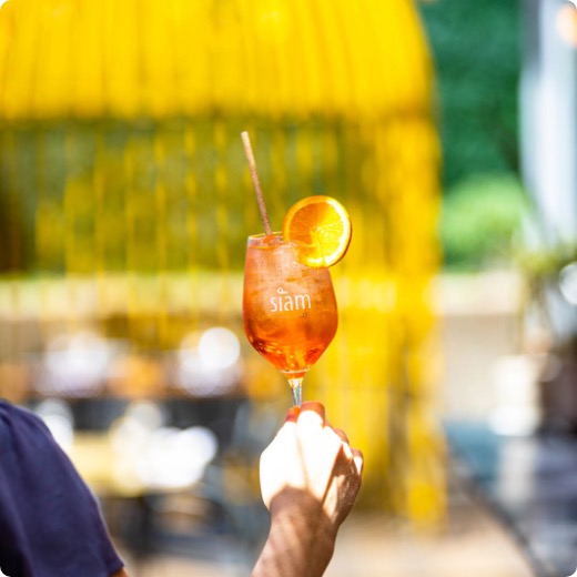 Un homme tient un Aperol Spritz sur la terrasse du Siam Dix30.