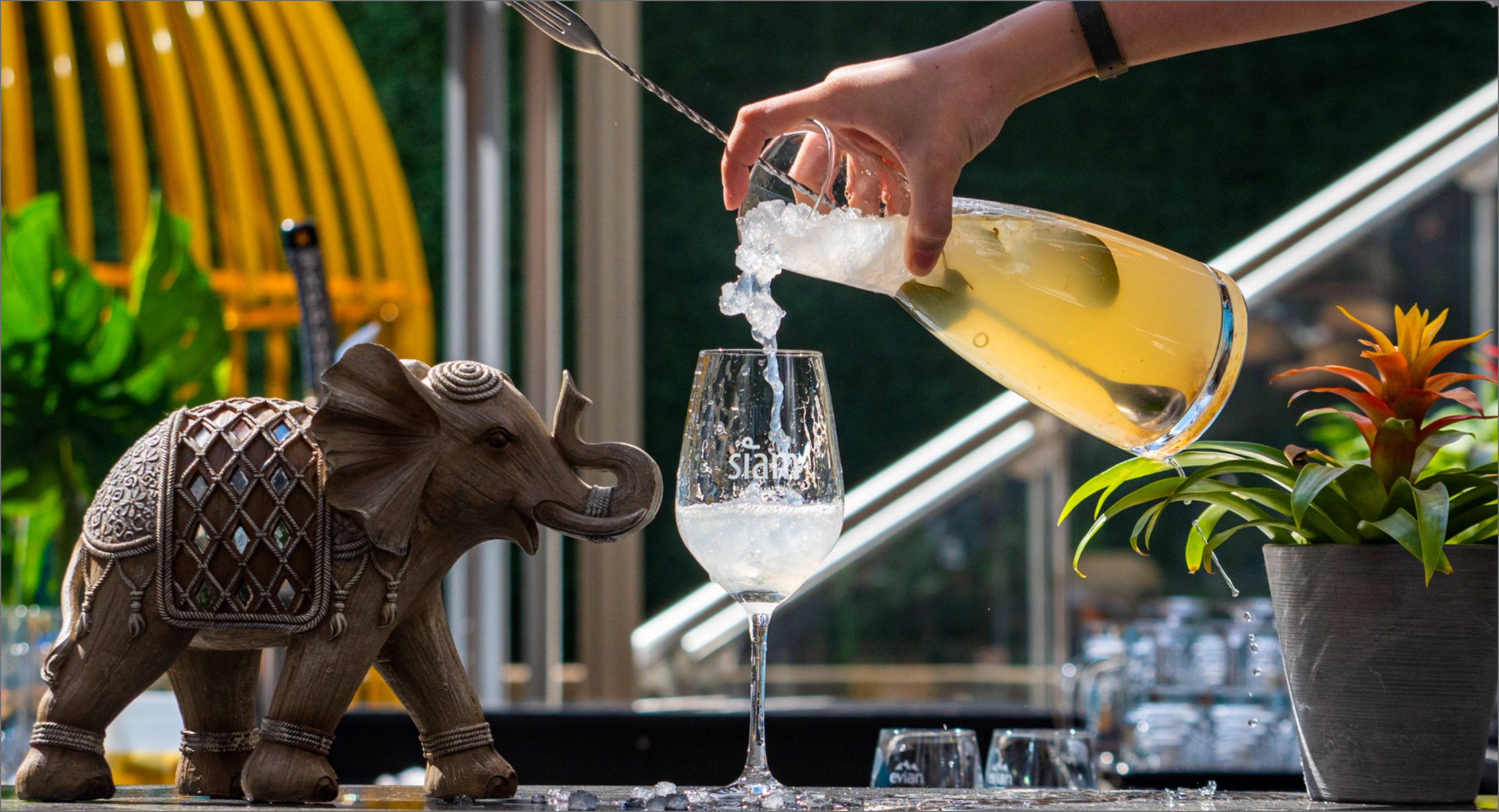 cocktail-terrasse-dix30.jpg Une main verse un cocktail fruité dans un verre avec une statue d'éléphant thaïlandais sur la terrasse du Siam Dix30.