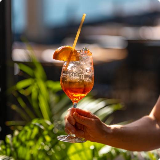cocktail-spritz-siam.jpg Une main tient un cocktail Spritz sur la terrasse du restaurant Siam Dix30 lors d'une chaude journée d'été.