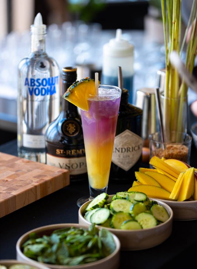 cocktail-couleurs-siam.jpg Un cocktail rose et jaune Phi Phi Island du restaurant Siam entouré de bouteilles d'alcool et de condiments.