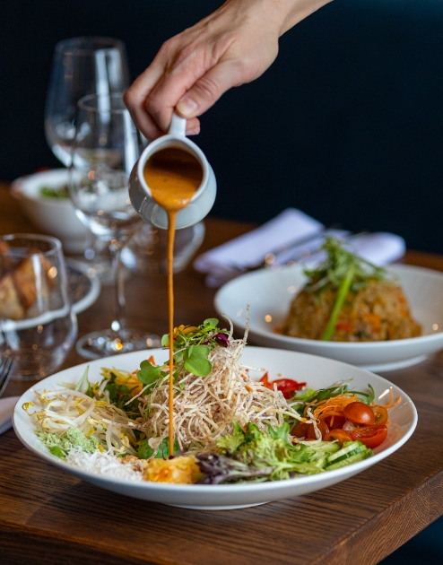 A person pours vinaigrette over a traditional Thai salad.