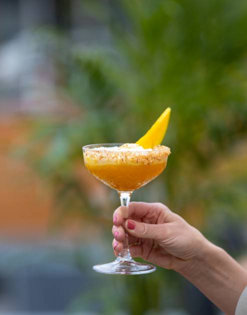 A hand holds a summer mango cocktail from Siam restaurant.