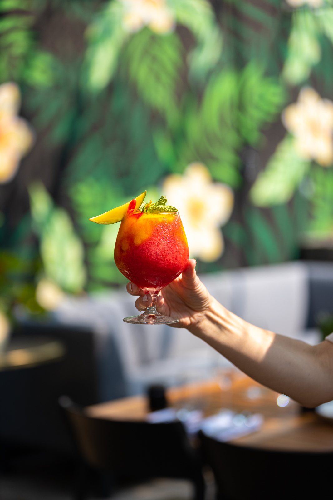 Une main tient un verre de cocktail rouge fruité sur une terrasse ensoleillée